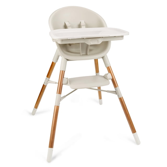 Skip Hop Baby High Chair 4-in-1 Convertible High Chair in oat with smooth plastic seat, adjustable white feeding tray, safety harness straps, wooden legs with white caps, and footrest, shown in front 3/4 view on white background.
