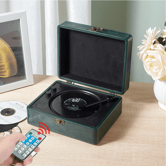 POINTERTECK CD Player with Bluetooth, a retro-style portable CD player resembling a green leather suitcase, displayed open on a wooden table. Features include built-in HiFi dual speakers, Bluetooth 5.0 connectivity, FM radio, AUX/USB support, and a headphone jack. A remote control is shown in use, and a CD is placed nearby. Ideal for home audio entertainment, desktop audio systems, and gifting.
