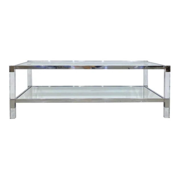 NERO COFFEE TABLE IN SILVER COLOR with a rectangular frame featuring two tempered glass shelves supported by transparent acrylic legs and silver steel accents, measuring 17.2"H x 50.5"W x 28.75"D, ideal for living room furniture and often used as a stylish display surface for books and decor.