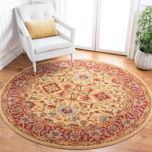 Safavieh Mahal Bentley Floral Bordered Area Rug round with classic Persian floral motifs in red, blue, and beige tones, power-loomed polypropylene for durability and easy care, placed on light hardwood floor beside a white armchair with a woven beige cushion in a bright room.