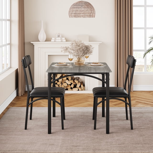 Dining Table Set for 2 with a square grey engineered wood tabletop and black metal frame, accompanied by two upholstered chairs with black cushions. Ideal for small spaces like apartments or studios, this space-saving set features a durable design and easy-to-clean surfaces. Displayed in a cozy dining room with a fireplace and natural light.