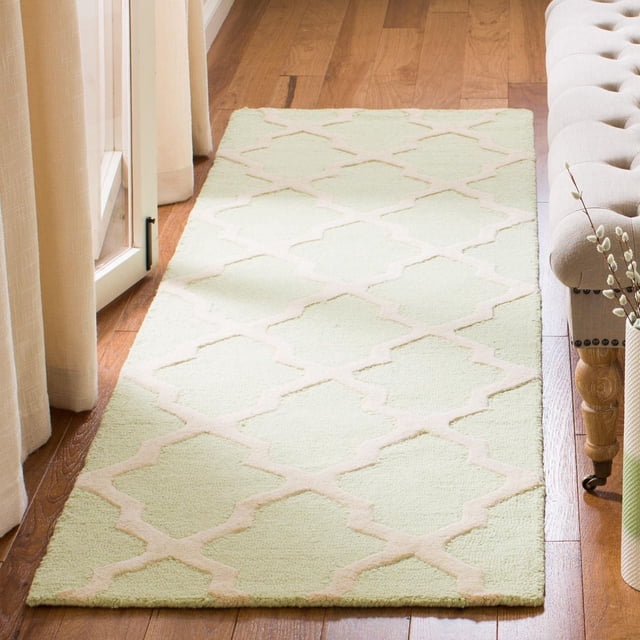 Safavieh Cambridge Liam Geometric Area Rug in soft green and beige featuring a hand-tufted wool texture with a geometric trellis pattern, placed on hardwood flooring beside a beige tufted bench and cream curtains, suitable for adding durable, textured style to home or office decor.