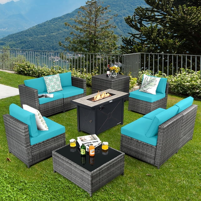 Gymax 9 PCS Patio Rattan Furniture Set with a 42-inch fire pit table, storage box, and turquoise cushions. Includes four armless sofas, two corner sofas, a coffee table with a tempered glass top, and a fire pit table with a 60,000 BTU propane burner. Constructed with durable PE rattan and a powder-coated steel frame, this set is ideal for outdoor spaces like patios, gardens, or backyards. Comes with waterproof covers, detachable cushion covers, and a bag of lava rocks. Displayed in a vibrant outdoor setting with a mountain backdrop.