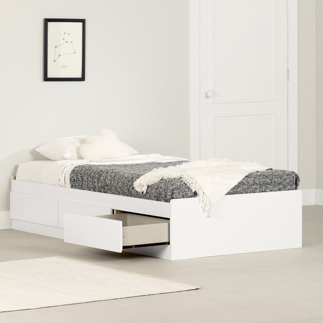 South Shore Vito Twin Mate's Platform Storage Bed with 3 Drawers in pure white, shown in a minimalist bedroom with one drawer open. The low-profile bed features clean lines, rounded edges, and three spacious storage drawers with flush inlaid handles and smooth metal slides on one side. It is dressed with a white pillow, cloud-shaped cushion, white sheet, dark grey textured blanket, and cream knitted throw. The background includes a white door, a framed Leo constellation print, and a light beige rug. This platform bed requires no box spring and is ideal for organizing bedding or clothes in small bedrooms.