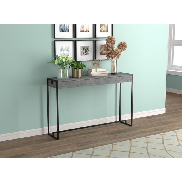 Safdie & Co. Table Console 47 L en Métal Ciment Noir Foncé avec un Dessus Étroit en Ciment Noir et un Cadre en Fer Forgé Noir, Positionnée contre un Mur et un Plancher de Bois Bleu Sarcelle Clair. la Table Tient des Plantes Vertes dans des pots en Verre et Dorés, des Livres Empilés et des Tiges Florales Séchées. Au-Dessus, six photos Botaniques Encadrées Sont Disposées en Deux Rangées. Cette Table Console Moderne et Minimaliste Est Idéale pour les Entrées Ou les Salons, Offrant une surface Élégante et un Soutien Robuste Tout en Complétant un décor
