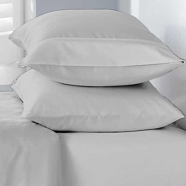 Basics Soft Pillowcase set with two stacked pillowcases in smooth, light-coloured 100% polyester fabric featuring a double-brushed texture, placed on a matching bed sheet in a softly lit bedroom corner, suitable for everyday restful sleep.