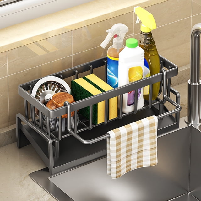 Staron Sponge Holder for Kitchen Sink, a grey ABS plastic kitchen sink caddy designed for kitchen organization and sink accessories. Measuring 9.05 inches by 4.33 inches by 3.93 inches, it features an inclined drainage system, towel hanging rod, and compartments for sponges, dish soap, brushes, and sink stoppers. Positioned on a kitchen counter next to a sink.