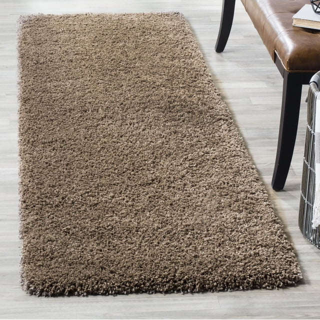 Safavieh California Tapis Shag Uni en Peluche avec un Épais Poil de Polypropylène de 4,5 Kg/m2, taupe, Forme Rectangulaire sur Plancher de Bois Clair, à Côté d'Un Banc en Cuir Brun et d'Un Panier Tressé, Offrant une texture Douce et Pelucheuse Idéale comme Tapis d'Accent pour la Maison.