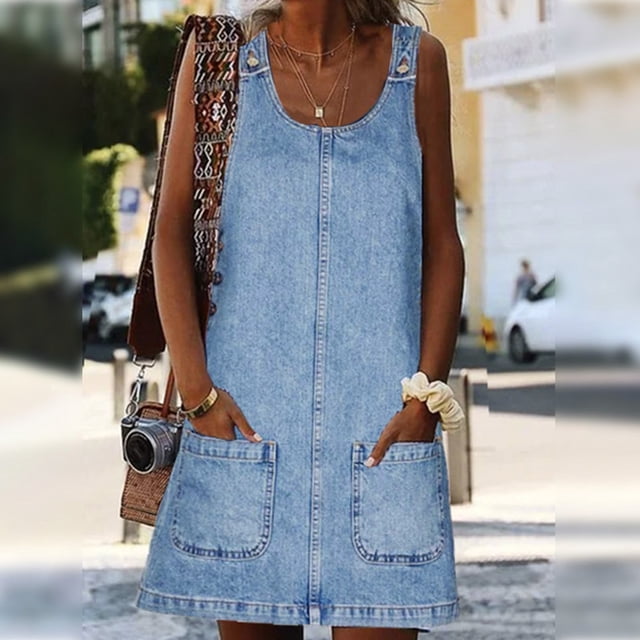 WILLBEST Robes pour Femmes pour Invitées de Mariage Jupe en Denim Populaire pour Femmes Aguichant et Cool Robe à Bretelles. une Robe en Denim Sans Manches avec Encolure Dégagée, Poches avant Appliquées et Coupe Décontractée, Idéale pour une Tenue Estivale Décontractée Ou comme Tenue d'Invitée de Mariage. le Modèle s'Accessoire avec des Colliers Superposés et un Sac Tissé, Photographié dans un Environnement Urbain Ensoleillé.