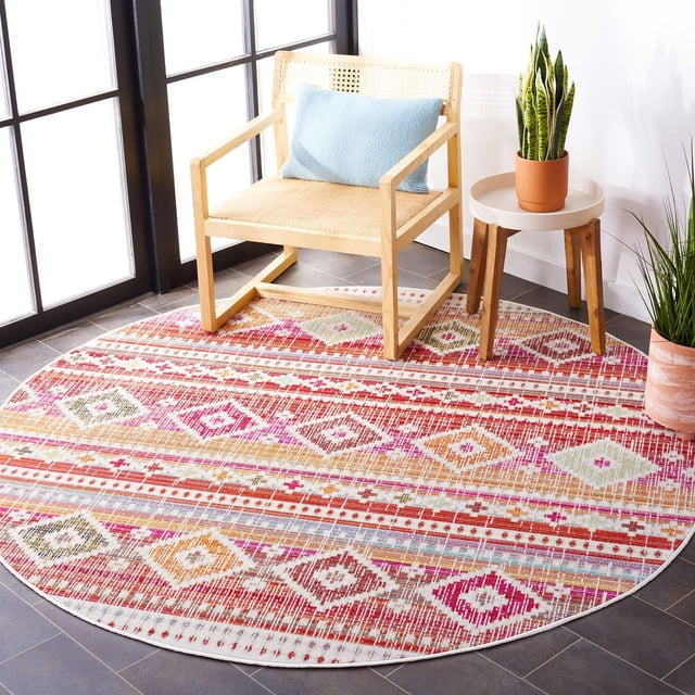 Safavieh Montage Tapis d'Extérieur Géométrique Seanan, Rond avec Motifs Géométriques Multicolores en Rouge, Rose, orange et beige, Tissé Mécaniquement pour Usage Extérieur, Posé sur un Plancher de Tuiles Foncées sous une Chaise en Bois Naturel avec Siège et Dossier en Canne Tressée, à Côté d'Une Petite table d'Appoint Ronde en Bois Tenant une Plante Serpent en Pot, Idéal pour patios Ou Vérandas.
