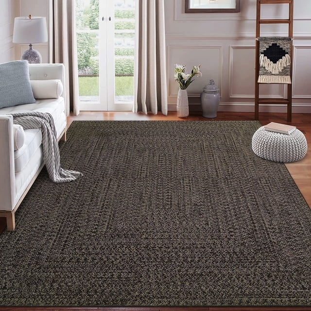 Garvee 5'x7' Area Rugs Braided Print Rug in brown, displayed in a cozy living room setting with a white sofa, pouf, and decorative ladder. This machine-washable indoor rug features a non-slip TPR rubber backing and a low 0.23-inch pile height, making it suitable for high-traffic areas like bedrooms, living rooms, and dining rooms. The braided print design adds a farmhouse aesthetic, while the durable polyester material ensures longevity and easy maintenance.