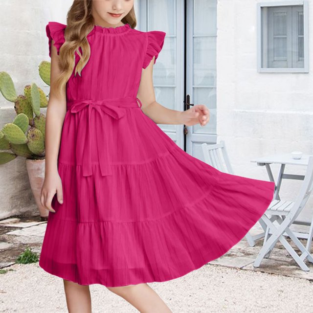XIMIN Robe d'Été Décontractée et Élégante à Col Rond pour Préadolescentes, avec Manches cap, Couleur Rose Unie et Manches à Volants, Coupe Trapèze. la Robe Comprend une Taille Haute avec une Ceinture Assortie et un Ourlet Évasé Fluide, Idéale pour les Fêtes Ou les occasions Formelles. Fabriquée en Mélange Respirant Coton-Polyester, Elle Assure le Confort et la Facilité de Mouvement. Présentée dans un Cadre Extérieur avec un patio Blanc et des cactus en Arrière-Plan.