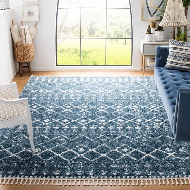 Safavieh Berber Fringe Robynne Tapis Shag Aztèque Bleu et Blanc avec une pile Peluche de 1,25 Po et des Motifs de Losanges Tribaux, avec des Bords à Franges, Placé dans un Salon Lumineux avec un sofa Capitonné Bleu, une Chaise Blanche et la Lumière Naturelle d'Une Grande Fenêtre. Il Convient Aussi pour Ajouter une Touche Bohème aux Coins de Lecture Ou aux Coins Douillets.