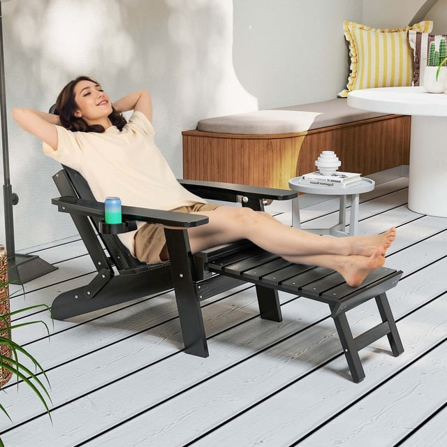 Costway Patio Adirondack Chair Chaise Longue Tout Temps en HIPS avec Repose-Pieds Rétractable Noir, Présentée dans un Décor de Patio Extérieur. la Chaise Présente un Dossier Réglable à 4 Niveaux, de Larges Accoudoirs et un Repose-Pieds Rétractable pour un Confort Accru. Fabriquée en Matériau HIPS durable et Résistant aux Intempéries avec des Vis en Acier Inoxydable, Elle Est Conçue pour Résister à Divers Climats. un Porte-Gobelet Rotatif Est Fixé à l'Accoudoir pour Plus de Commodité. la Chaise Est Pliable pour un Rangement et un transport Faciles, la Rendant Idéale pour les patios, les Cours Arrière Ou les Jard