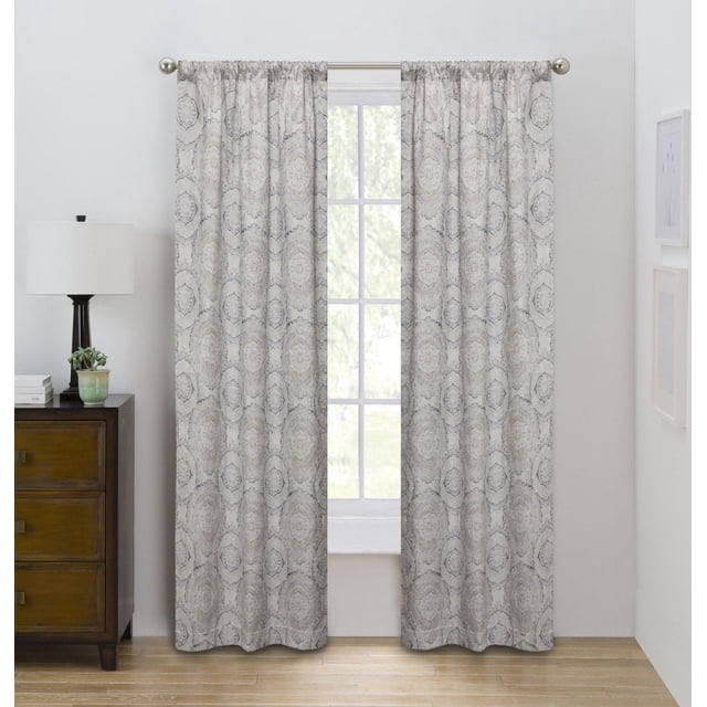 Eclipse Draft Stopper 63" room darkening rod pocket window curtains panel in neutral circular medallion pattern, featuring insulating fleece fuse backing to block cold air and filter light, hanging on silver rod in a bright room with wooden floor and dark wood nightstand with lamp and plant.