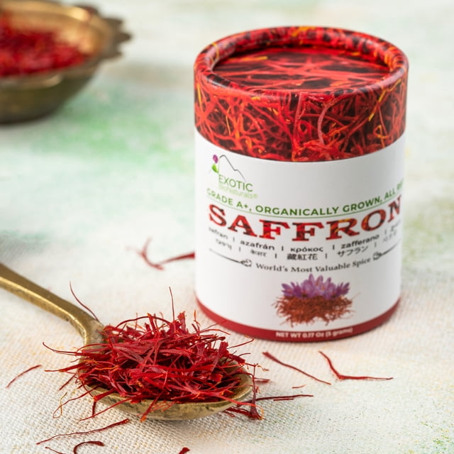 EXOTIC BioNaturals Saffron (28.3 Grams / 1 ounce) in a cylindrical, air-tight container labeled as Grade A+ Super Negin saffron. The container features vibrant red saffron threads on the design and multilingual text. A golden spoon filled with vivid red saffron threads is placed in the foreground, showcasing the rich color and texture of the spice. The background is softly blurred, emphasizing the saffron's premium quality and freshness.