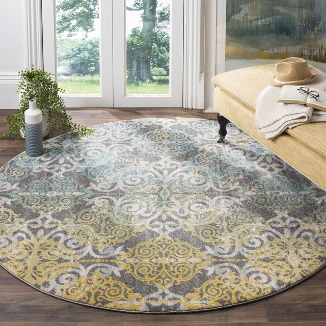Safavieh Evoke Keith Tapis Damassé, Rond avec un Motif Damassé dans des Tons Bleu, Jaune et Gris Atténués, Fait de Frise en Polypropylène Tressée Mécaniquement, Posé sur Plancher de Bois Franc Près d'Un Banc Rembourré beige avec un Chapeau, des Lunettes et un Livre, à Côté d'Un vase Bleu et Blanc avec Plante Traînante Verte Près des Portes en Verre.