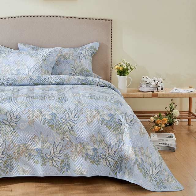 Kingrest Cotton Quilt Set Twin Size, Lightweight Pattern Comforter Set, Oversized Bedspread Coverlet Quilted Bedding Set displayed in a bedroom setting. The quilt features a vibrant floral pattern in soft pastel tones on a light blue background, with a chevron quilted texture. The set includes a matching pillow sham, styled on a beige upholstered headboard and complemented by a wooden bench with decorative items like flowers and books. Ideal for year-round use, this bedding set combines comfort, durability, and style.