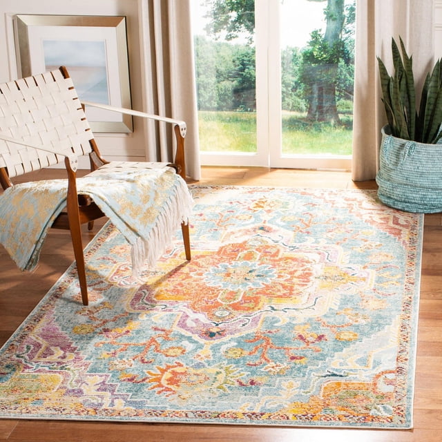 SAFAVIEH Crystal Debra Floral Area Rug with close cut pile and intricate floral medallion patterns in vivid orange, blue, yellow, and purple, power loomed from synthetic yarns, placed on hardwood floor in a bright room with a white woven chair draped with a blue and beige fringed throw and a snake plant in a blue basket near large glass doors.