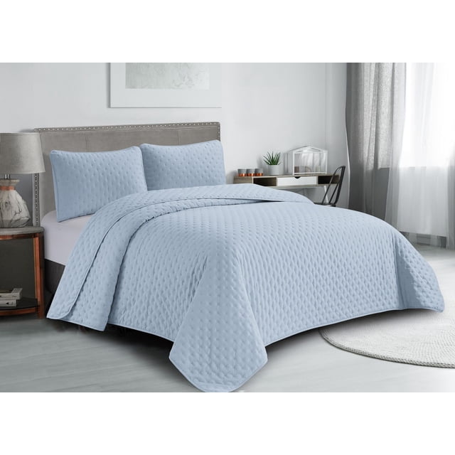 Swift Home Ultra Soft Pinsonic Quilt Set in light blue on a queen bed with matching pillow shams, featuring a textured pinsonic pattern in soft microfiber fabric. The lightweight, hypoallergenic bedding offers all-season comfort. The room includes a grey upholstered headboard, wooden nightstand with marble lamp, and a desk with decor near a window with sheer and grey curtains.
