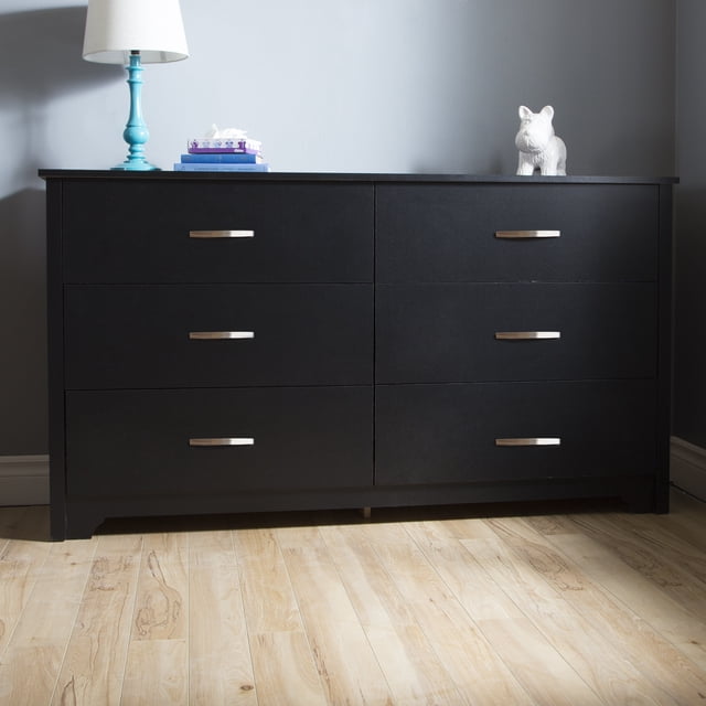South Shore Fusion 6-Drawer Dresser for Adult in pure black with six spacious drawers featuring slim metal handles and molded edges, designed in a contemporary style with straight lines and a clean-cut bottom, placed against a grey wall on a light hardwood floor, topped with a turquoise lamp, books, and a white ceramic dog figurine, ideal for organized bedroom storage.