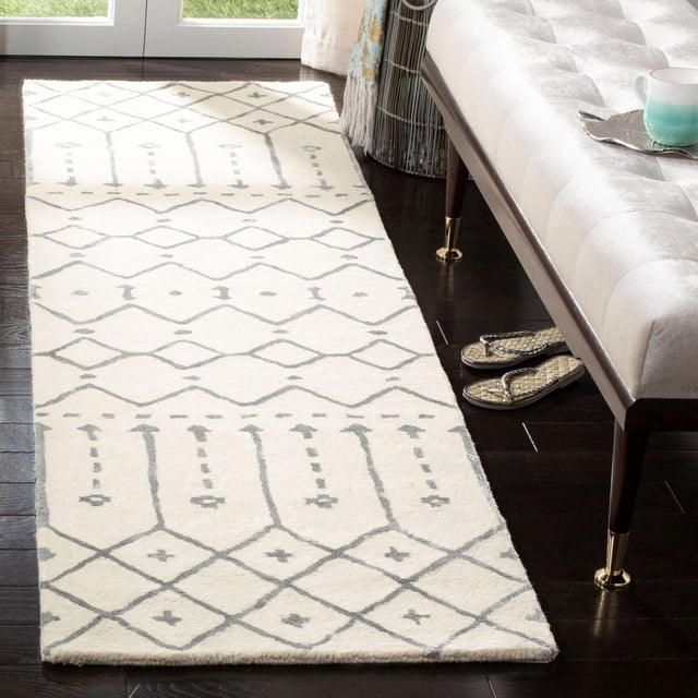 Safavieh Himalaya Darin Geometric Area Rug runner featuring a cream 100% hand-loomed wool base with light grey geometric diamond and arrow patterns, placed on dark hardwood flooring beside a beige tufted bench with gold-capped legs near a glass door, ideal for modern hallway or entryway decor.