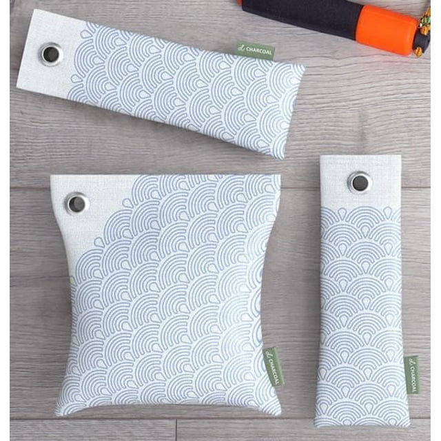 Vie Oli Bamboo Charcoal Air Purifying Bags in three sizes with white hemp fabric and light gray wave pattern, each with a metal grommet and green 'Charcoal' tag, placed on a light wood surface, ideal for moisture absorption and freshening small spaces.