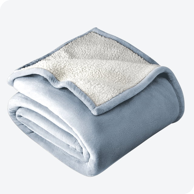 Bare Home Couverture de Lit en Sherpa Peluche Bleu Poussiéreux, Format Simple/Simple TG, Mesurant 90” x 66 Pouces. Cette Literie Légère Présente un design Réversible avec une Micro-Polaire Douce d'Un Côté et une Doublure Sherpa Peluche de l'Autre, Offrant un Confort Maximal et des Propriétés Hypoallergéniques. Pliée Soigneusement sur un Fond Gris Pâle.