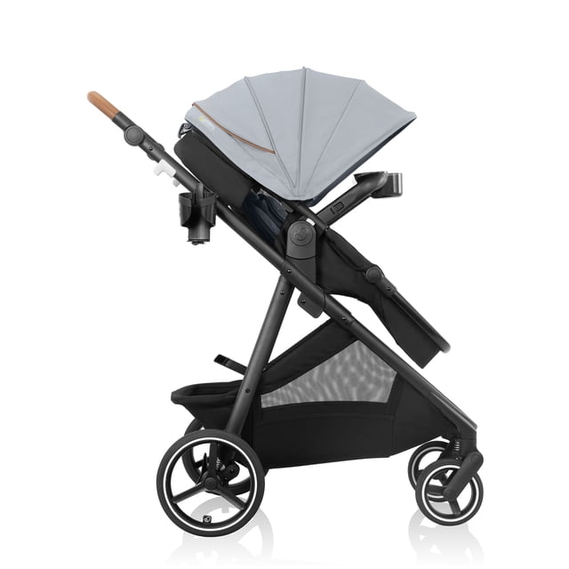 Evenflo Shyft Intuiti+ Stroller with Green & Gentle Fabric (3-55 lbs) in side profile with light grey expandable UPF 50+ canopy, black modular frame featuring all-wheel suspension, large rear and smaller front rubber tires, brown leatherette adjustable handle, child snack tray, parent cup holder, and spacious black mesh storage basket.