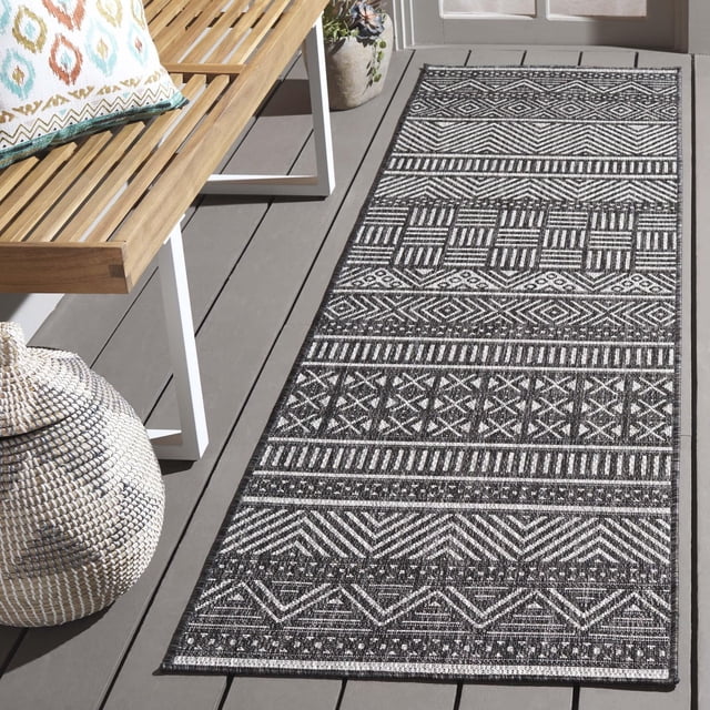 SAFAVIEH Beach House Jolanta Tapis Géométrique Intérieur/extérieur Gris et Noir avec des Motifs Géométriques Variés Incluant des Rayures, des Losanges et des chevrons, Posé sur une Terrasse en Bois Grise à Côté d'Un Banc en Bois avec un Coussin à Motifs et un Panier Tressé, Idéal pour une Utilisation durable Intérieure Ou Extérieure.
