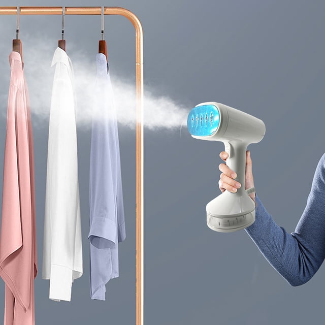 Dormitory Portable Artifact Iron, Household Handheld Small Hanging Iron, Clothes Steam Ironing Machine in white, emitting steam while held by a person. The compact, foldable design includes a 140ml water tank for convenient use. Ideal for travel, it is shown alongside neatly hung shirts in pink, white, and blue on a copper clothing rack.