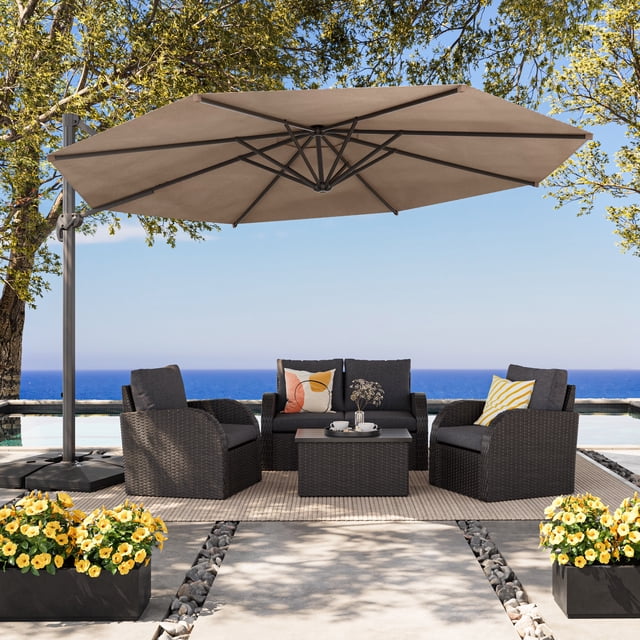 CorLiving 11.5ft Deluxe Tilting and Rotating Offset Patio Umbrella with aluminum frame and brown canopy shading a dark brown woven outdoor seating set with two armchairs, a loveseat with decorative cushions, and a coffee table on a beige rug beside a pool overlooking the ocean, surrounded by trees and yellow flowering planters.