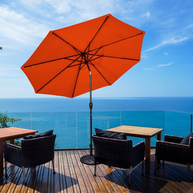 Costway Parasol Solaire de Patio 10 Pi à DEL, Marché, Acier Inclinable avec Manivelle, Extérieur, Orange, Nouvel Ensemble sur une Terrasse en Bois Surplombant l'Océan. le Parasol Présente une Canopée en polyester Orange Vibrante avec protection UV et Propriétés Déperlantes, Soutenu par 8 Nervures en Acier. un Panneau à Énergie Solaire sur le Dessus Alimente 24 Lumières DEL Écoénergétiques. le Mât en Acier Comprend un Mécanisme d'Inclinaison et de Manivelle pour un Ajustement Facile. Support Non Inclus.