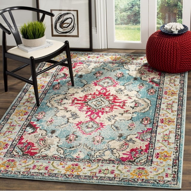 Safavieh Monaco Toria Traditional Area Rug featuring a power-loomed polypropylene weave with high and low loop pile, displaying a folkloric Persian medallion pattern in red, cream, blue, and yellow tones on a hardwood floor beside a black wooden chair and red knitted pouf, suitable for adding Bohemian-chic style to accent spaces.