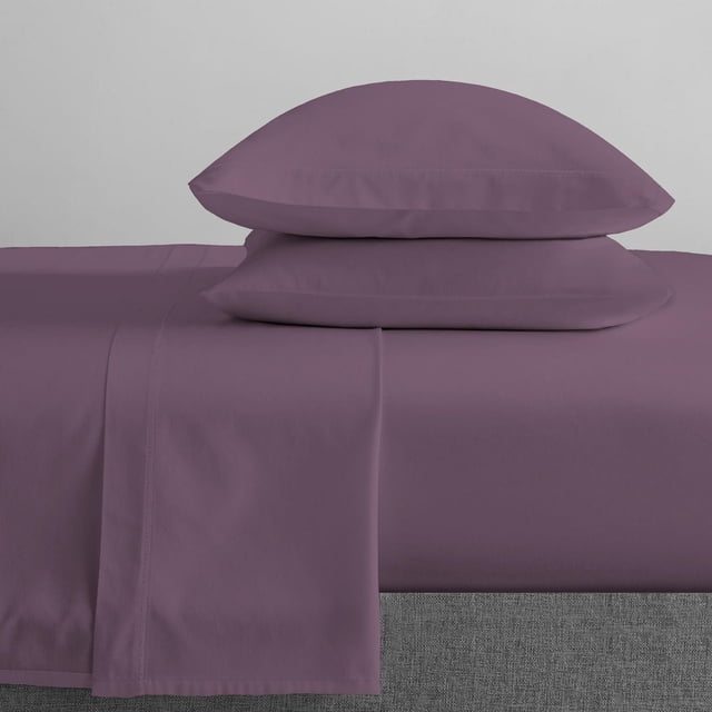 Johnson Home 300 Thread Count Combed Egyptian Cotton Sheet Sets in muted purple, showing a flat sheet and two matching pillowcases stacked on a bed with a grey upholstered base, highlighting the soft, breathable fabric designed for durability and year-round comfort in bedroom settings.