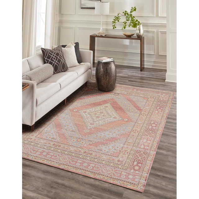 ECARPET Poppy Traditional Area Rug with soft pastel and warm neutral geometric patterns placed on grey wood flooring in a living room featuring a beige sofa with patterned cushions, a dark textured drum side table with books, and a wooden console table with a lamp and vase, ideal for high-traffic spaces.