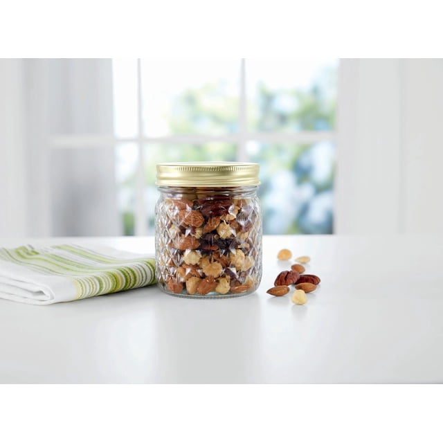MS Pot en Verre Matelassé de 500 ml avec Couvercle Hermétique Doré, Rempli de Noix Mélangées Incluant des Amandes, des Pacanes et des Noisettes, Placé sur une surface Blanche à Côté d'Un Essuie-Tout de Cuisine Plié à Rayures Blanches et Vertes, avec un Fond de Fenêtre Lumineux, Convient au Rangement des Aliments et à l'Organisation du Garde-Manger.
