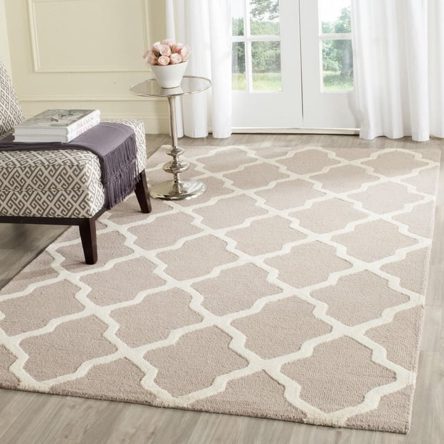 Safavieh Cambridge Liam Geometric Area Rug in beige with white trellis pattern, hand-tufted wool with plush cut and loop pile, on light wood flooring in a bright room with sheer curtains, next to a patterned armchair and silver side table with pink roses, ideal for modern home or office decor.