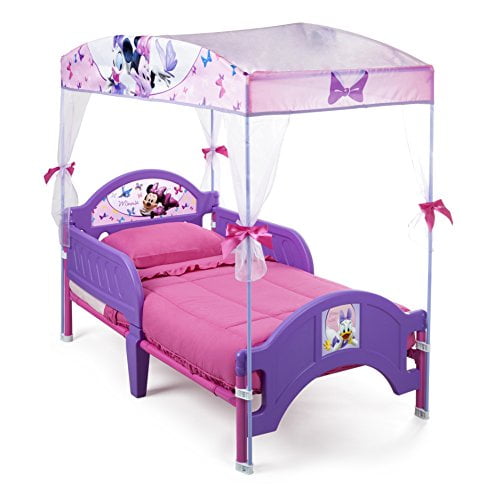 Delta Children's Products Minnie Mouse Canopy Toddler Bed featuring a multicolour design with purple and pink tones. The bed includes a sheer canopy with ribbon ties, Minnie Mouse and Daisy Duck decals, and a low-to-the-ground frame for easy access. It also has removable side rails for added safety. Suitable for a child's bedroom.
