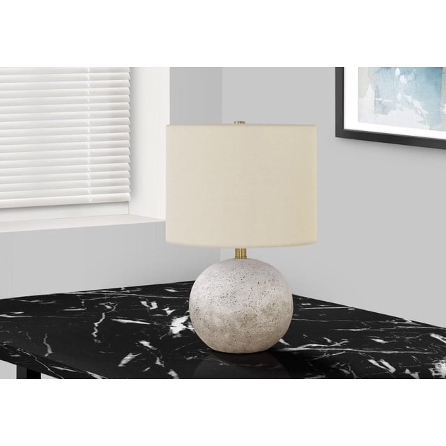 Monarch Specialties Lighting 20"h table lamp with a grey concrete textured spherical base and ivory linen drum shade with gold finial, placed on a black marble surface near a window with white blinds and framed abstract wall art, suitable for living rooms or bedrooms.