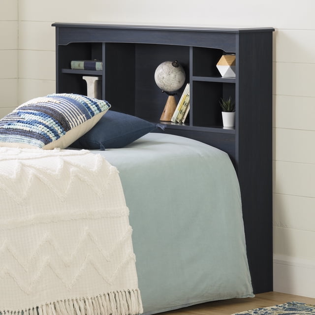 South Shore Navali Twin Bookcase Headboard with Storage in Blueberry, shown attached to a twin bed with light blue bedding and white textured throw. It features five open fixed shelves for bedside storage, holding a globe, books, a small plant, and geometric decor. The modern nautical design includes a cable management hole for tidy wires, suitable for bedroom organization.