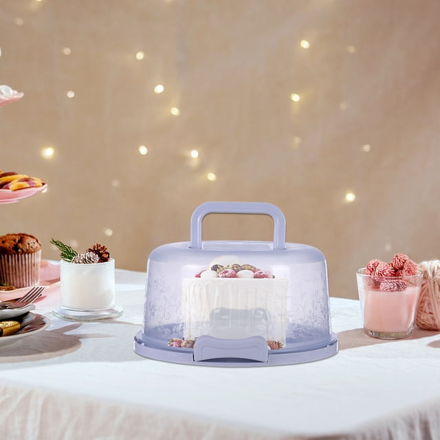 Riforla Portable Cake Box Cake and Cupcake Cake Holder Container for Cake Pie Food Storage C One Size. A round, clear plastic cake box with a purple base and handle, featuring an elegantly designed cover with floral patterns. The box securely holds a decorated cake inside, showcasing its design while providing protection. Dual sturdy clamps lock the lid in place for airtight storage and safe transport. The container is placed on a table surrounded by desserts and festive decor, ideal for storing and transporting cakes, cheesecakes, and other baked treats.