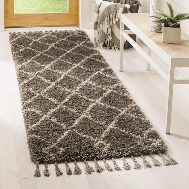 Safavieh Moroccan Fringe Lavern Geometric Shag Area Rug runner featuring plush synthetic yarns with a grey and cream geometric diamond pattern and fringed tassels on both ends, placed on a light hardwood floor near a wooden door and white console table with a plant, ideal for adding comfort and tribal style to entryways or hallways.