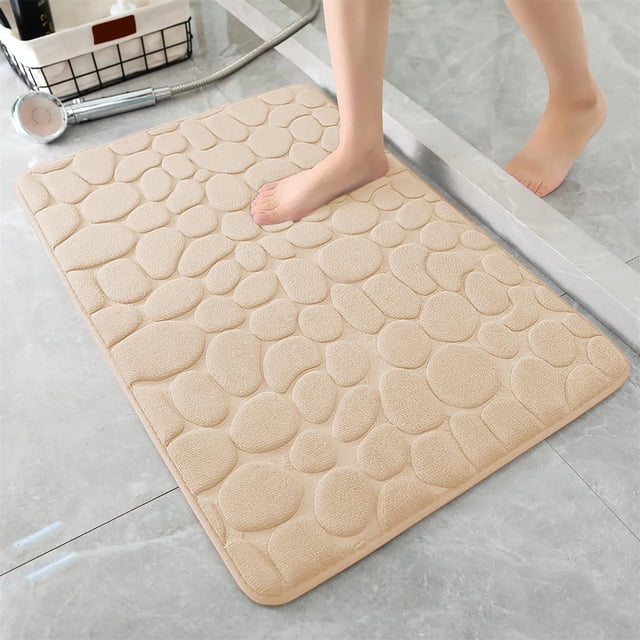 Holiday Zanvin Rugs, 1pc memory foam bath rug embossed bathroom mat in beige with a textured stone-like pattern. Designed for bathroom use, it features water absorbent, washable material, and non-slip backing. A foot is stepping on the soft, thick mat placed on a tiled bathroom floor, ideal for bathroom rug sets.