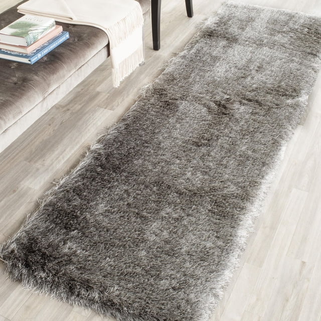 Safavieh Paris Darwin Plush Shag Area Rug with a thick, plush grey shag pile in a runner shape on light wood flooring beside a grey upholstered bench with a cream throw and books, suitable for adding texture and warmth to modern home spaces.