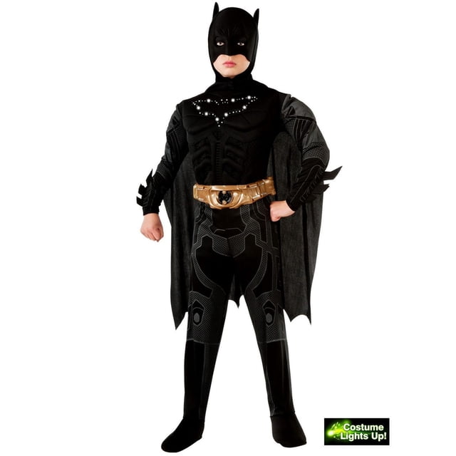 The Dark Knight Trilogy Light-Up Batman Boy's Costume with a black polyester jumpsuit featuring printed armor details, attached boot tops, spiked gauntlets, a molded gold utility belt with a black Batman emblem, a cape, and a headpiece with pointed ears. The chest has a light-up Batman symbol powered by a button cell battery, suitable for Halloween superhero dress-up.