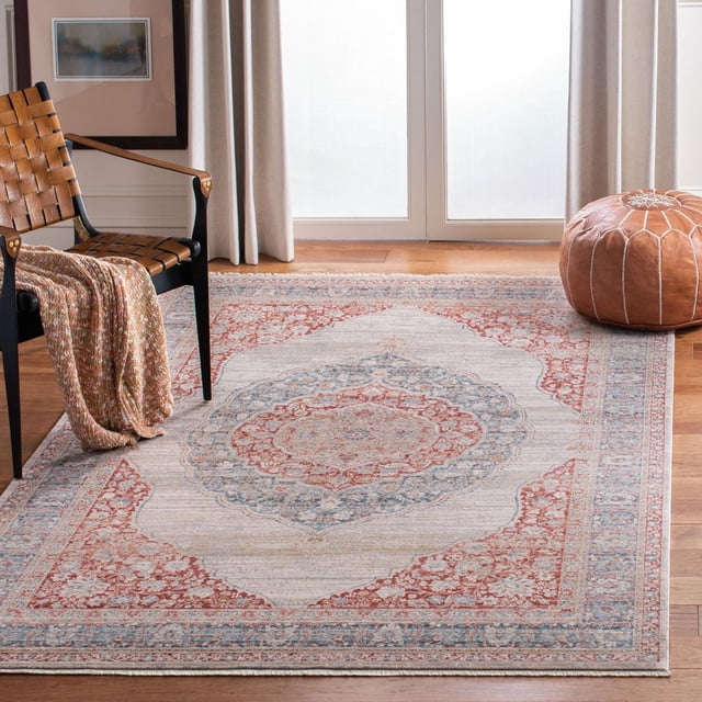 SAFAVIEH Kenitra Flowers Floral Bordered Polyester Area Rug on hardwood floor in a bright room, featuring a central floral medallion in ruby red and soft blue with beige and ivory tones, framed by intricate floral borders, paired with a woven leather chair and a brown leather pouf, ideal for enhancing classic style and comfort in living spaces.