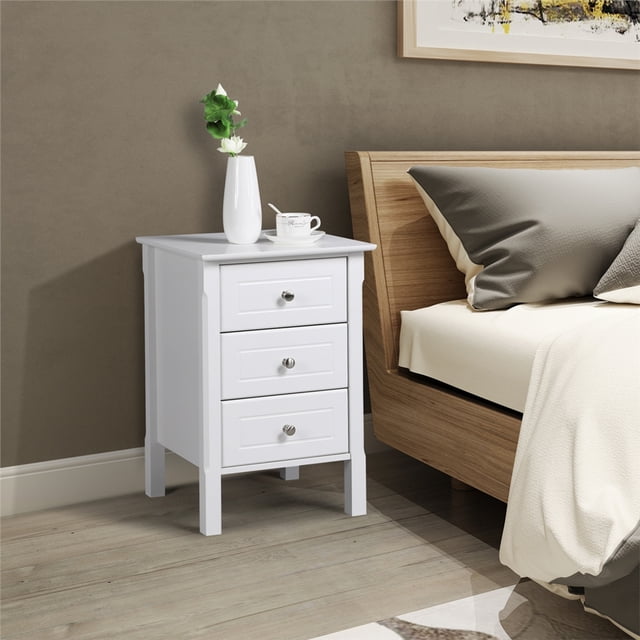 Yaheetech Table de Nuit Moderne à 3 Tiroirs pour Chambre, Salon, Blanc, Positionnée dans une Chambre Contemporaine à Côté d'Un Cadre de Lit en Bois. la Table de Nuit Présente une Finition Blanche, Trois Tiroirs à Glissement Fluide avec Boutons Ronds Argentés et d'Élégants Détails de Pieds Sculptés. Son Plateau Carré de 16 Pouces Accueille un vase avec des Fleurs et une Tasse à Thé, Offrant un Grand Espace de Rangement et d'Exposition.