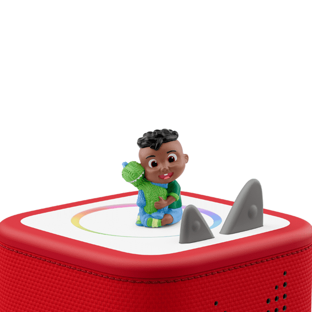 tonies Cocomelon: Cody Audio Play Figurine showing a multicolour figurine of a child in a green shirt and blue shorts hugging a green dinosaur, seated on a red Toniebox audio player with a white top panel featuring a circular rainbow design and two grey ears.