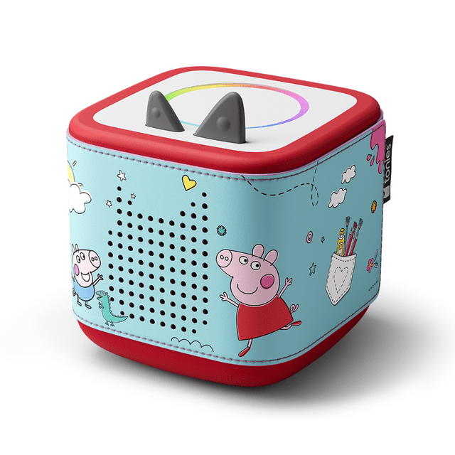 tonies Toniebox 2 Étui : Peppa Pig Montrant une Vue Inclinée aux 3/4 d'Un Étui audio en Forme de Cube en Bleu Pâle avec des Personnages Peppa Pig, des Nuages, des Cœurs et une Pochette avec des Outils d'Art. le Étui s'Ajuste Solidement sur la base Toniebox 2 Rouge, avec des Trous pour Haut-Parleurs à l'Avant et Deux Oreilles Grises sur le Dessus. Il a des Bords Cousus et une Étiquette tonies Noire, Conçu pour l'Électronique Éducative et les Jouets
